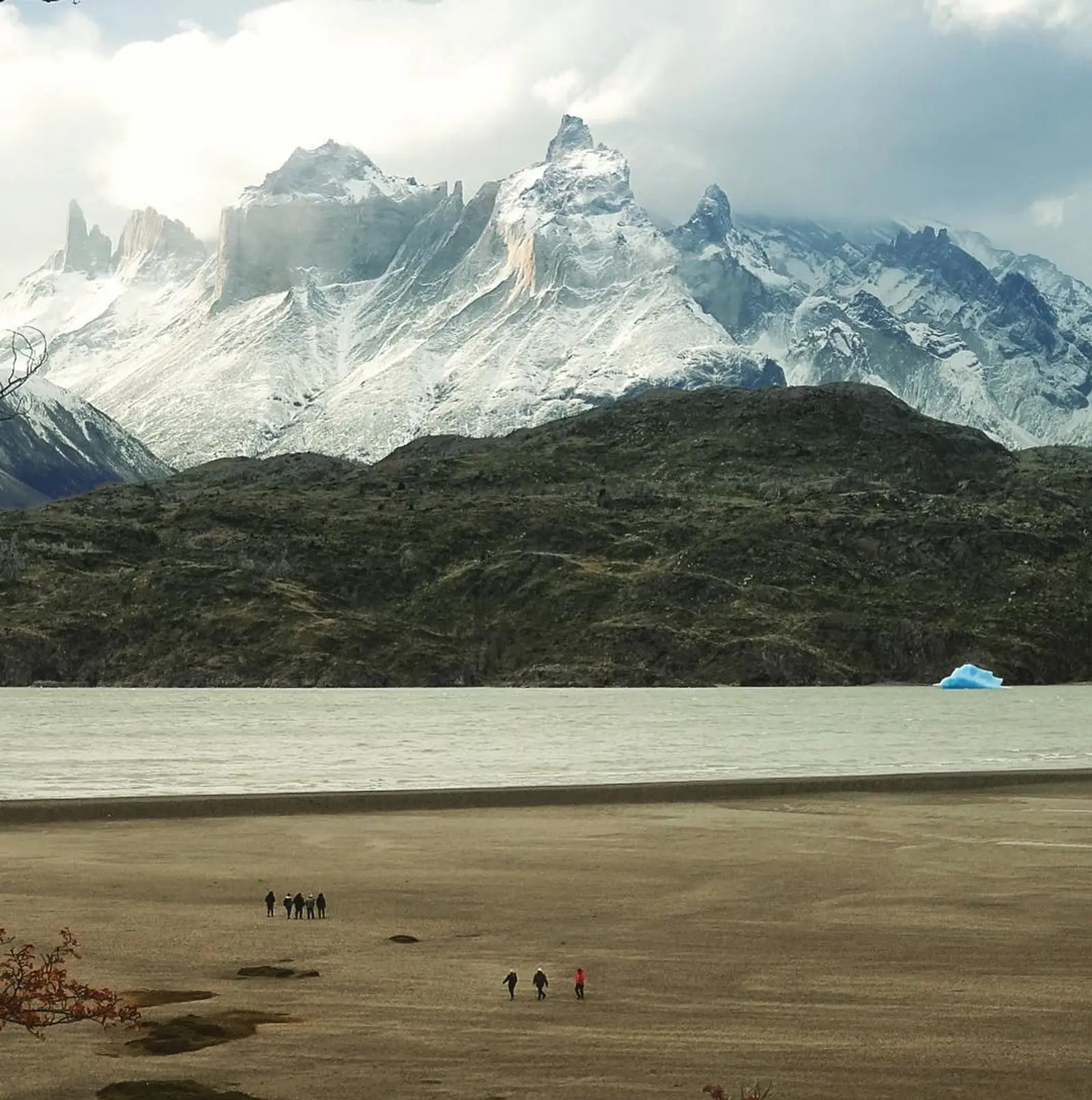 Personas caminando en playa patagónica, con témpanos de hielo y montaña de fondo
