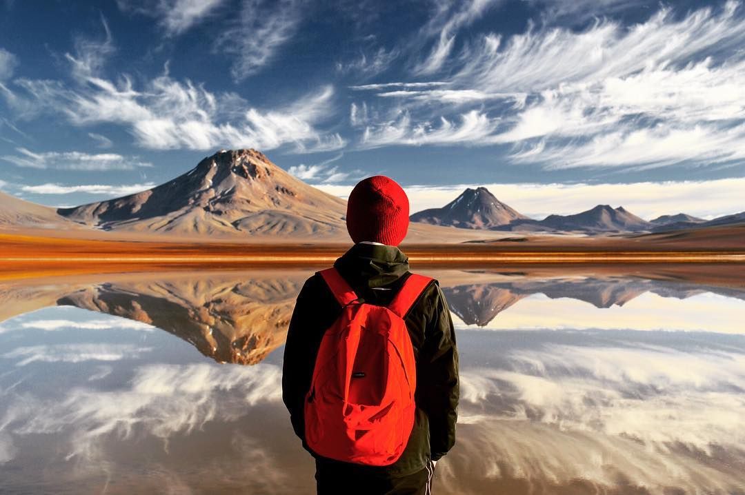 Joven parado frente a laguna y montañas