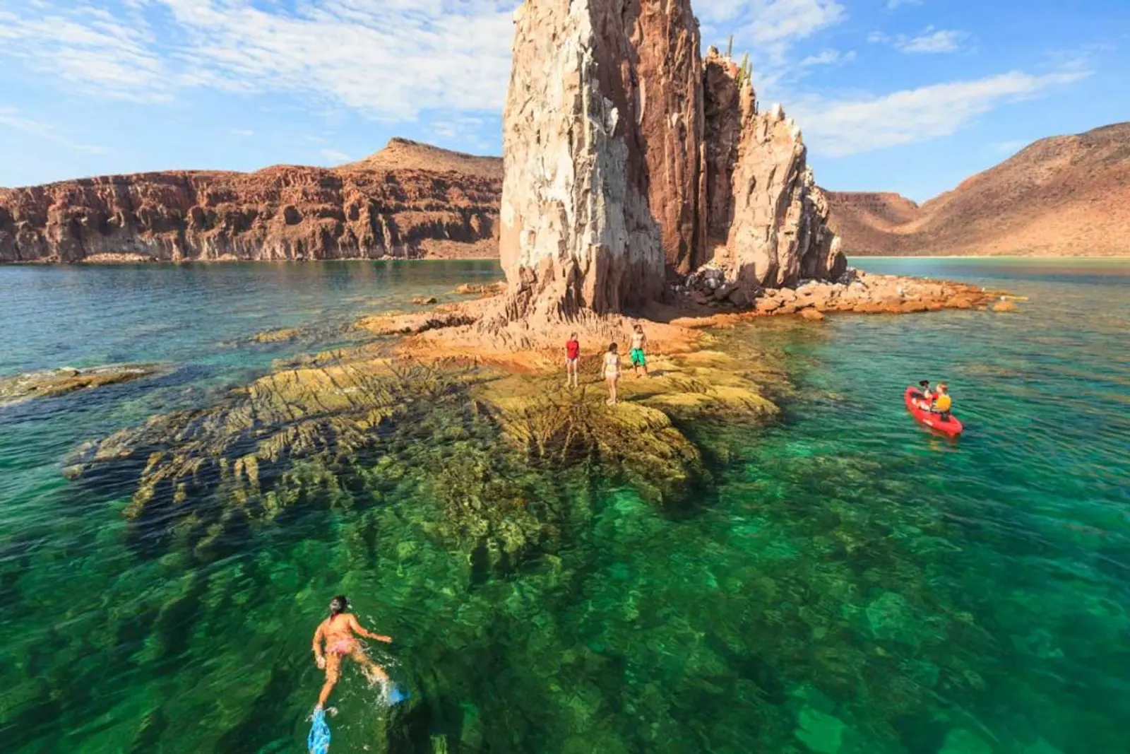 Personas nadando en el mar alrededor de gran roca